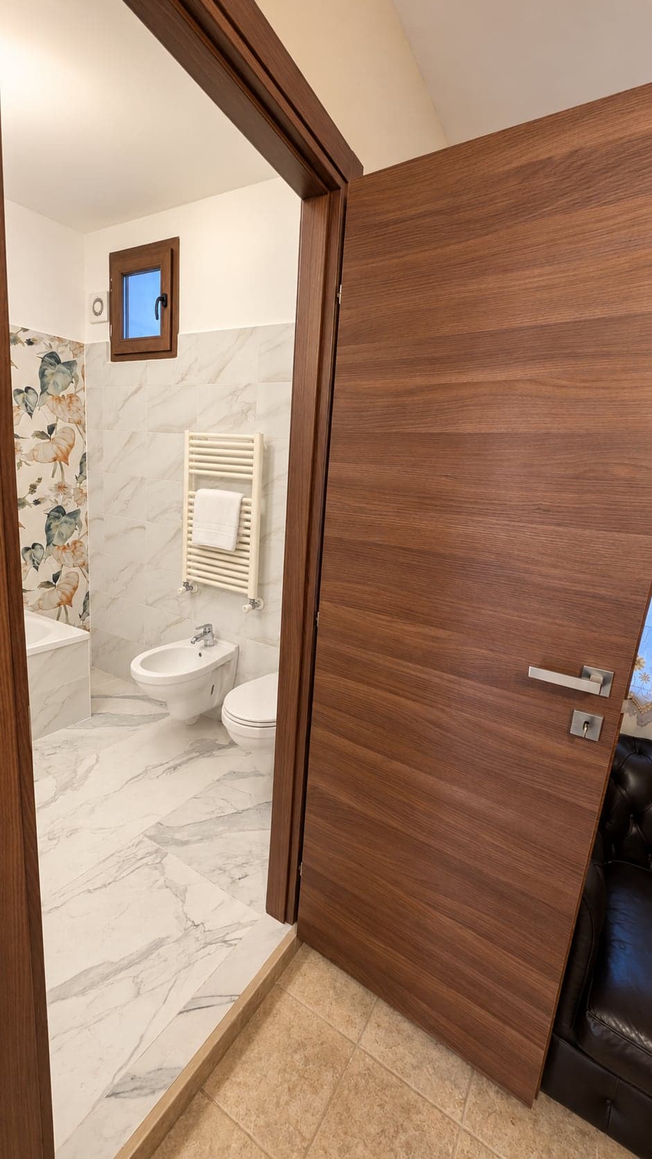 Bagno con piastrelle effetto marmo, vasca, sanitari e scaldasalviette