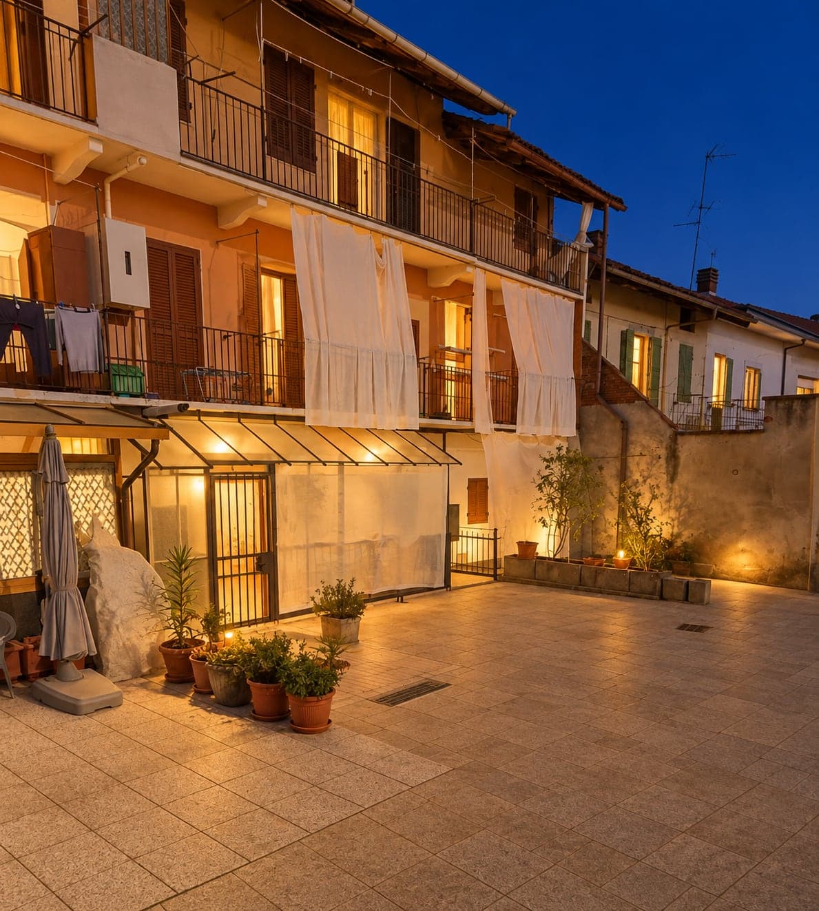 La corte di Corte House al tramonto, con piante in vaso e luci calde